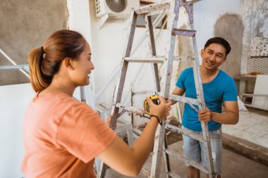 Asyalı genç çift, evin çatısını onarmak için birlikte merdiven taşıyor.