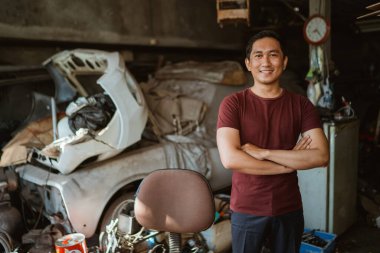 Eski bir garajda kollarını kavuşturmuş yakışıklı genç bir tamirci.