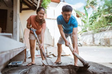 Yeni evli kadınlar ve erkekler bir ev inşa etmek için marangozluk aletlerini kullanarak çimento karışımı yapıyorlar.