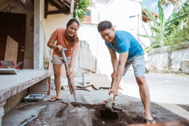 Genç Asyalı çift ev yapmak için kürek ve çapa kullanarak çimento karışımı yapıyor.