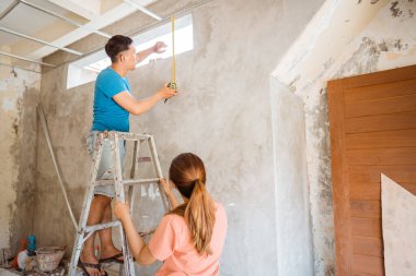 Koca yeni bir ev inşa ederken havalandırma deliğinin genişliğini ölçerken merdivene tırmanır.