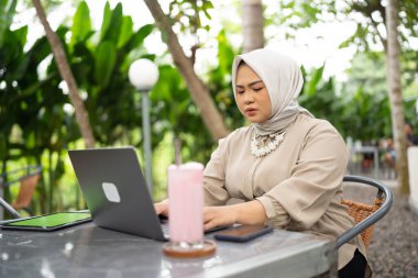Kafede çalışan tesettürlü iş kadını. Laptop ve tablet kullanıyor. Ciddi bir ifadeyle.