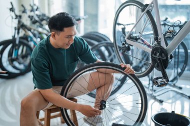 Genç Asyalı bir adam bisiklet dükkanında çalışırken aksları tamir ediyor.