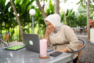 Bir kafede çalışırken dizüstü bilgisayar ve tablet kullanarak gülen tesettür işkadını.