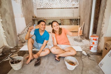 Genç çift, inşaat halindeki yeni bir evde cep telefonuyla selfie çekmek için oturuyor.