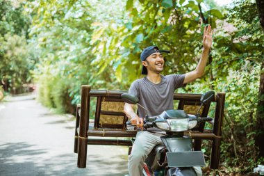 Dost canlısı adam bambu koltuklar satıyor. Sokakta bir motosiklette bambu sandalye taşıyor.