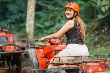 beautiful asian women looking at the camera with her smile while riding the atv at tracking area clipart