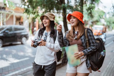 Yol kenarında kameralar ve haritalar taşıyan iki turist beldesi arayan iki gezgin kız.