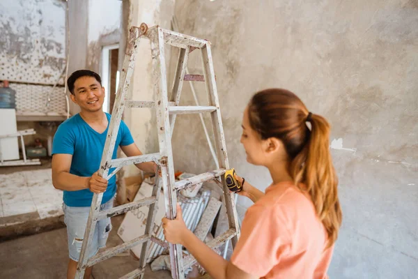 Asian couple moves stepladder to fix ceiling of new house