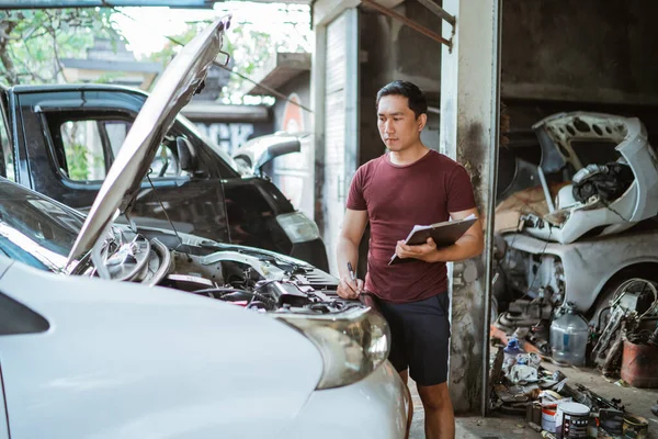 Νεαρός Μηχανικός Στέκεται Κοιτάζοντας Μια Μηχανή Αυτοκινήτων Έτοιμος Γράψει Τις — Φωτογραφία Αρχείου