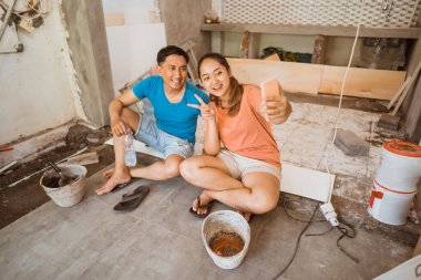 Genç bir çift cep telefonuyla selfie çekerken kendi evlerini yenilerken birlikte vakit geçiriyorlar.