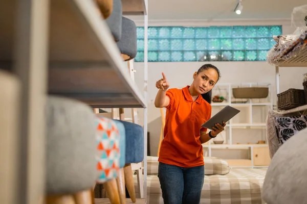 Female supervisor counts furniture products on a shelf while checking with a tablet at a furniture store