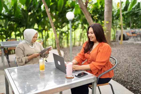 two women working together in a cafe using laptop and tablet