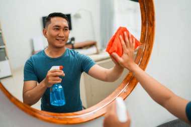 Asyalı adamın yansıması aynayı temizler ve parlatır.