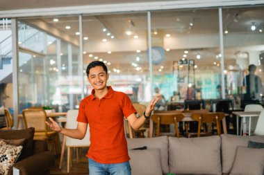 Kırmızılı erkek tezgahtar. Heyecanlı bir ifadeyle bir mobilya dükkanında duruyor.