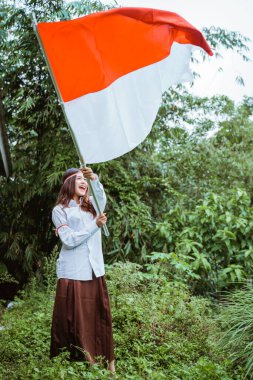 Beyaz gömlekli ve kahverengi etekli güzel bir Asyalı kadın bayrağı elinde sallıyor ve gülümsüyor.