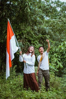 Yakışıklı bir adam kolunu sıktı ve elinde Endonezya bayrağı olan güzel bir kadın ormanda yan yana duruyordu.