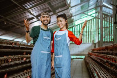 Gülümseyen girişimci çift, kümes hayvanları çiftliğinde kafeslere yakın duran bir şey sunuyor.