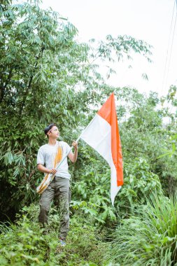 Beyaz tişörtlü yakışıklı bir Asyalı. Sarong ayakta duruyor. Elinde Endonezya bayrağı var.