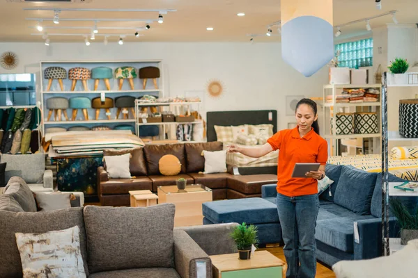 female shop assistant checking with data on a tablet while working at a furniture store