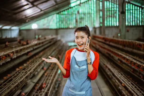 Asian woman entrepreneur chats on a cell phone call with hand presenting at poultry farm