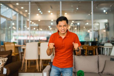 Kırmızılı esnaf, mobilya dükkanında dikilirken asık suratlı sinirli.