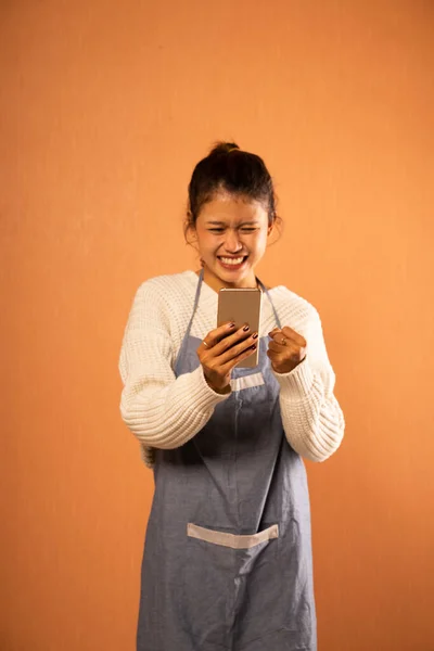 Збуджена Азіатська Дівчина Носить Фартух Дивлячись Мобільний Телефон Ізольованому Фоні — стокове фото