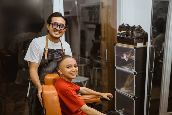 亚洲男性理发师和他的顾客摆出友好的姿势拍照 图库图片