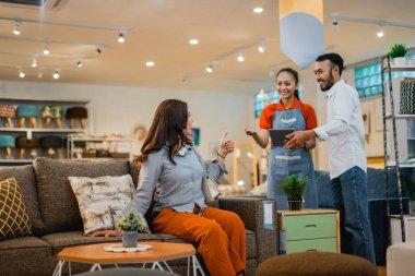 Bayan müşteri koltukta oturmaya çalışırken garson da mobilya mağazasındaki yeni mobilya ürünlerine bakıyor.