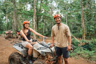 Asyalı kadın üzerinde otururken mutlu Asyalı adam ATV 'nin önünde duruyor.