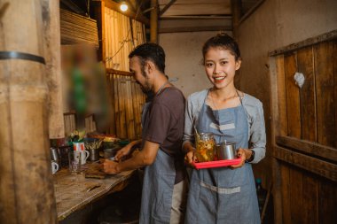 Tezgahtar kadın mutfak arka planında geleneksel içkileri servis ederken elinde bir tepsi taşıyor.
