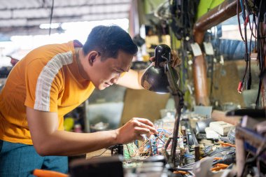 Teknisyen atölyenin ışığı altında tornavida kullanarak elektronik aletleri test ediyor.