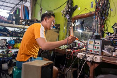 Asyalı erkek teknisyen bir benzin istasyonundaki elektronik devreyi tamir ederken lehim makinesi kullanıyor.