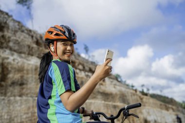 Bisiklete binen ve telefon kullanan bayan bisikletçi kameraya, dikiz aynasına bakıyor.