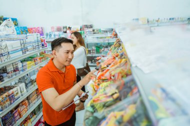 Erkek mağaza asistanı, minimarket 'te çalışırken listedeki öğeleri kaydeder.