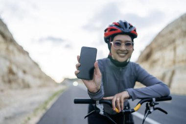 Bisikletli kadın ve elinde arka planı bulanık boş bir ekran telefonu var.