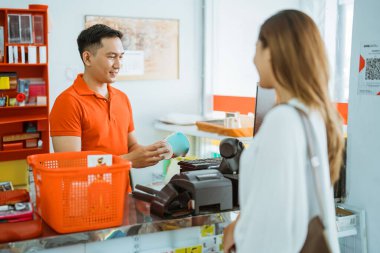 Erkek esnaf, bayan müşterilerin minimarket kasiyerlerden alışveriş yaptığı barkod taraması için mal bulundurur.