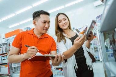 Erkek tezgahtar ve kadın işyeri sahibi minimarket bir rafta eşyaları birlikte kontrol ediyorlar.