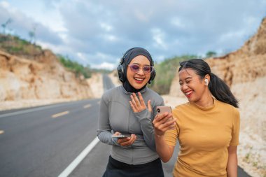tesettürlü kadın ve bayan arkadaş telefon kullanıyor, gülüyor ve birlikte koşuyorlar.