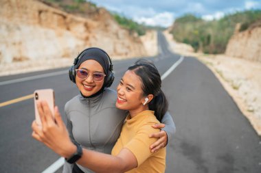 Atletik kadın tesettürlü bir arkadaşla telefon kullanıyor onu kucaklıyor, koşu konsepti uyguluyor.