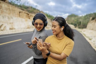 İki atletik kadın dışarıda çalışırken işaret işareti yaparak telefon kullanıyor.