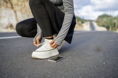 Kadın, ayakkabı bağını yanında telefonla bağlayan, eğri büğrü bir pozisyonda.