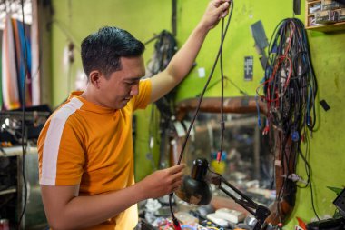 Asyalı Tamirci, elektronik tamir odasında çalışırken bağlanmak için kablo seçti