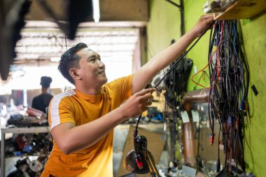 Asyalı tamirci elektronik tamir odasındaki duvardan bir kablo alıyor.