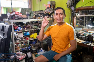 Gülümseyen elektronik tamircisi elektronik servis istasyonunda iyi bir el hareketi gösteriyor.