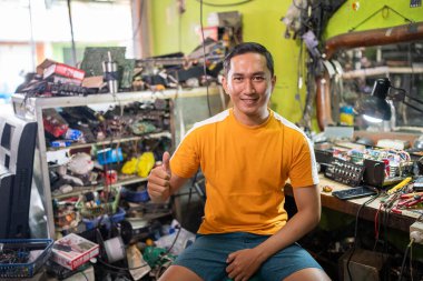 Erkek elektronik tamircisi elektronik servis istasyonunda baş parmak göstererek oturur.