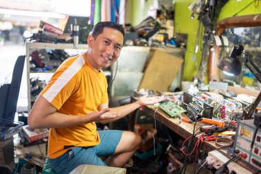 Benzin istasyonunda çalışırken el hareketi yapan Asyalı erkek teknisyen.