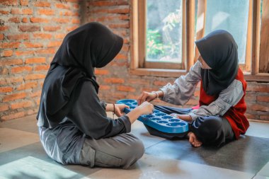 hijab girl holding plastic board for playing indonesian traditional games called congklak clipart