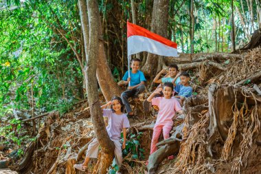 Asyalı çocuklar ellerinde Endonezya bayrağı, selamla el hareketi yapıyorlar.