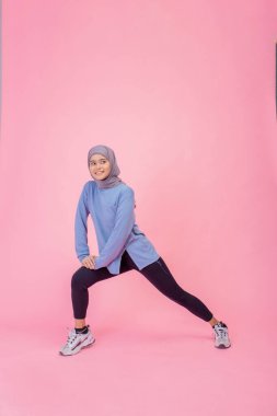 Şık giyinmiş genç bir kadın canlı pembe bir arka planda kendine güvenerek poz veriyor.